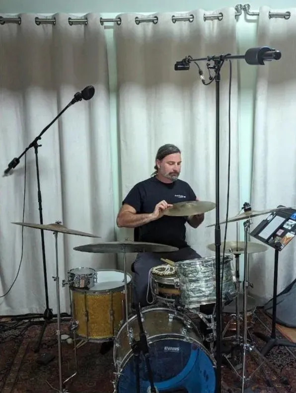 Drummer at a vintage kit with overheads in front of white curtains
