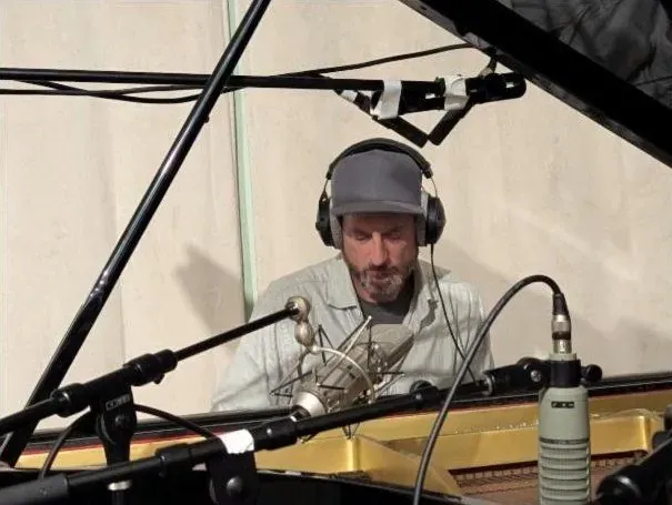 Pianist in headphones and a cap at the grand, mics over the strings