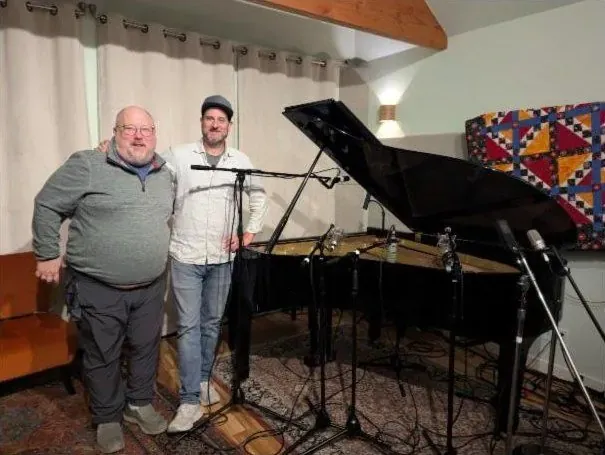 Two men standing beside the grand piano with mic stands around it