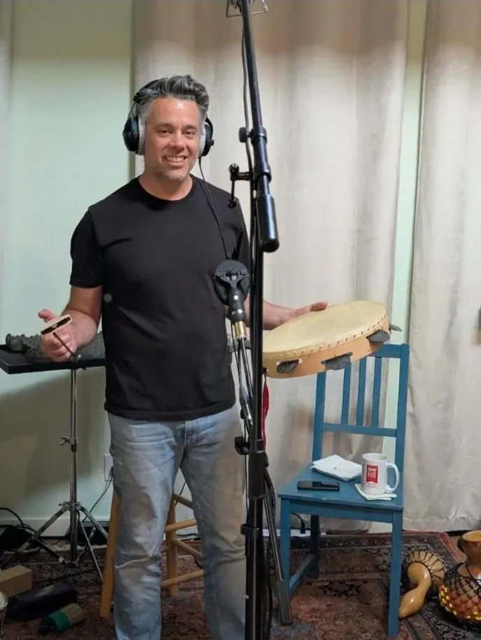 Percussionist in headphones holding a frame drum and a shaker at the mic