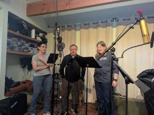 Three singers at music stands in front of a gold condenser mic