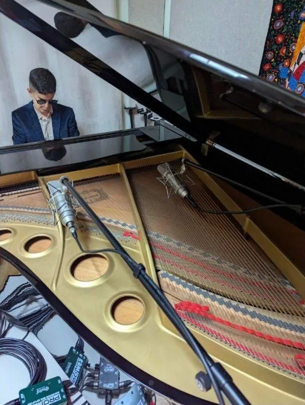 Pianist in sunglasses at the grand piano, two condenser mics over the strings