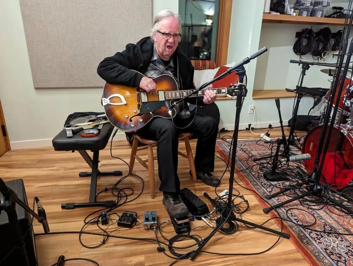 Guitarist playing an archtop with a pedalboard at his feet